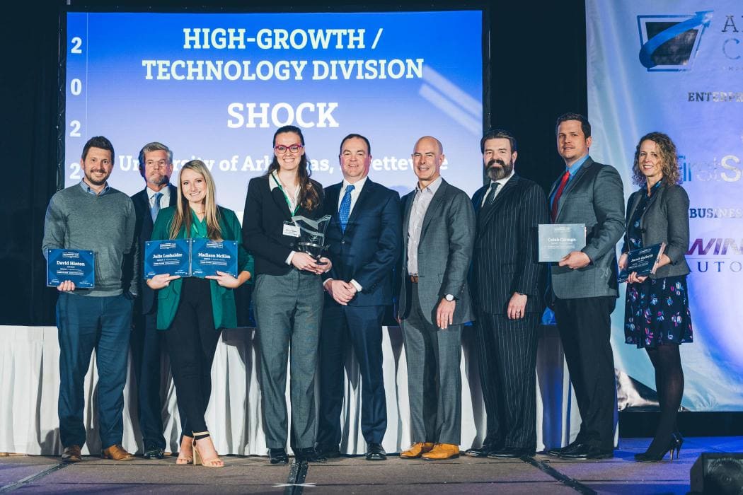 Nine people stand on stage holding awards, posing for a photo in front of a sign that reads “High-Growth / Technology Division SHOCK.”.